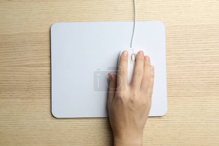 Woman using wired computer mouse on wooden table, top view. Space for text