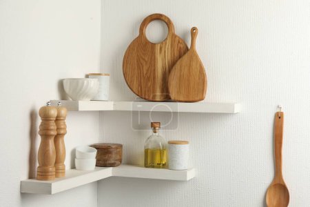 Foto de Tableros de madera para cortar, vajilla y utensilios de cocina en estantes blancos - Imagen libre de derechos