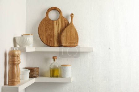 Foto de Tableros de madera para cortar, vajilla y utensilios de cocina en estantes blancos, espacio para texto - Imagen libre de derechos