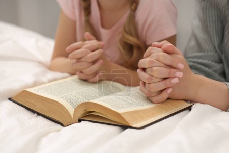 Photo for Girl and her godparent praying over Bible together indoors, closeup - Royalty Free Image