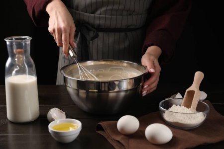 Woman making dough with whisk in bowl at table, closeup