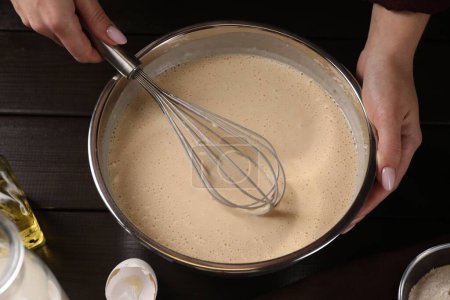 Femme faisant de la pâte avec fouet dans un bol à table, gros plan