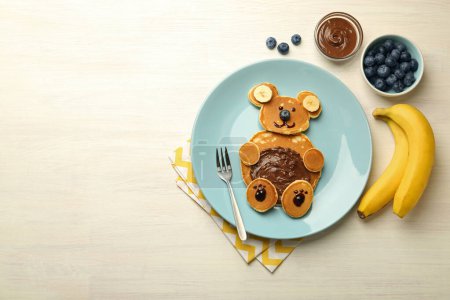 Foto de Servicio creativo para niños. Placa con oso lindo hecha de panqueques, arándanos, plátanos y pasta de chocolate en la mesa de madera clara, la puesta plana. Espacio para texto - Imagen libre de derechos
