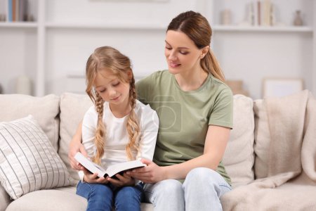 Photo for Girl and her godparent reading Bible together on sofa at home - Royalty Free Image