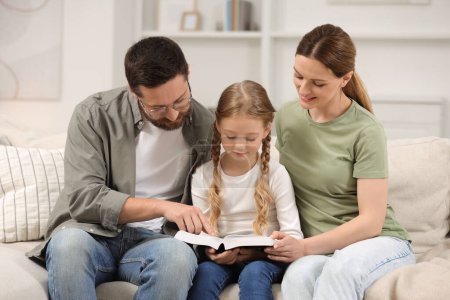 Photo for Girl and her godparents reading Bible together on sofa at home - Royalty Free Image