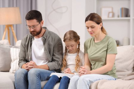 Photo for Girl and her godparents praying together on sofa at home - Royalty Free Image