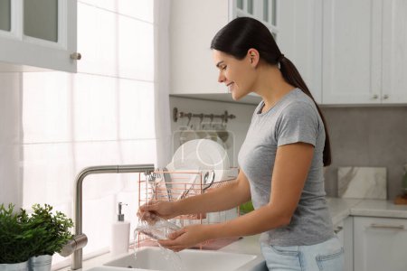 Foto de Mujer feliz lavado de vidrio en el fregadero en la cocina - Imagen libre de derechos