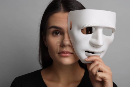 Foto de Concepto de personalidad múltiple. Mujer con máscara sobre fondo gris - Imagen libre de derechos
