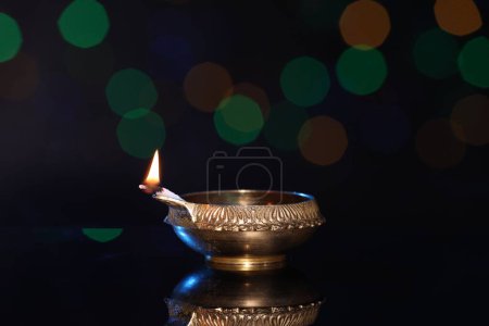 Photo for Lit diya on dark background with blurred lights, space for text. Diwali lamp - Royalty Free Image