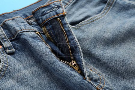 Téléchargez les photos : Jeans avec mouche déboutonnée sur fond bleu clair, gros plan. Concept exhibitionniste - en image libre de droit