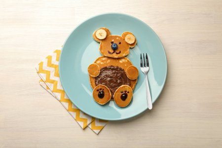 Foto de Servicio creativo para niños. Placa con oso lindo hecha de panqueques, arándanos, plátanos y pasta de chocolate en la mesa de madera ligera, vista superior - Imagen libre de derechos