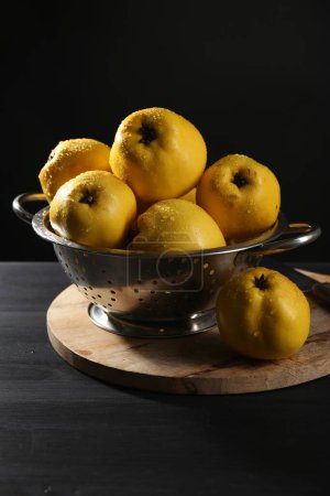 Tasty ripe quinces with water drops in metal colander on black wooden table