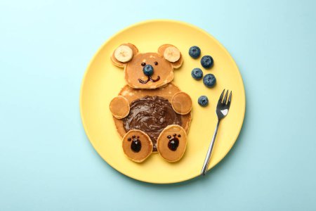 Foto de Servicio creativo para niños. Placa con oso lindo hecha de panqueques, arándanos, plátanos y pasta de chocolate en la mesa azul claro, vista superior - Imagen libre de derechos