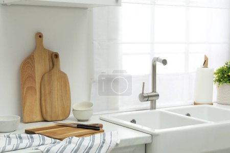 Foto de Tableros de corte de madera, tazones, cuchillo y toalla en encimera blanca cerca del fregadero en la cocina - Imagen libre de derechos