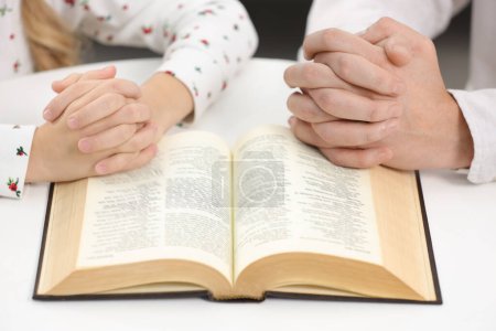 Photo for Girl and her godparent praying over Bible together at table indoors, closeup - Royalty Free Image