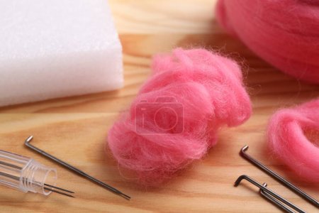 Pink felting wool and needles on wooden table, closeup