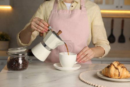 Frau gießt aromatischen Kaffee aus Mokka-Kanne in Tasse an weißem Marmortisch, Nahaufnahme