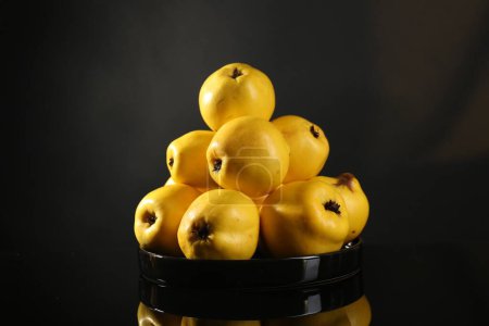 Tasty ripe quinces in bowl on black mirror surface