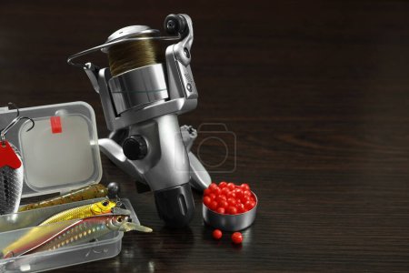 Photo for Fishing tackle. Spinning reel, bait and lures on dark wooden background, space for text - Royalty Free Image