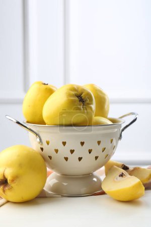 Tasty ripe quinces and metal colander on white wooden table