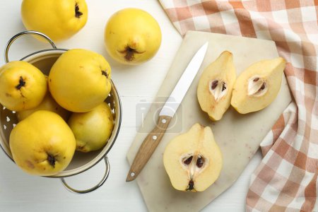 Tasty ripe quinces, metal colander and knife on white wooden table, flat lay