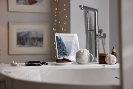 Téléchargez les photos : Plateau en bois blanc avec tablette, produits de spa et bougies allumées sur la baignoire dans la salle de bain - en image libre de droit