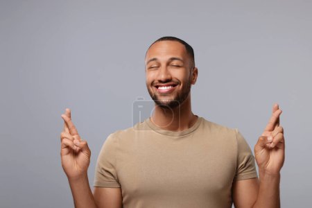 Foto de Hombre feliz cruzando sus dedos sobre fondo gris - Imagen libre de derechos