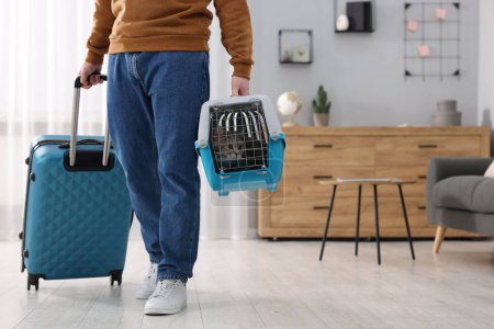 Téléchargez les photos : Voyage avec animal de compagnie. Homme tenant transporteur avec chat mignon et valise à la maison, gros plan. Espace pour le texte - en image libre de droit