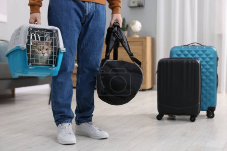 Téléchargez les photos : Voyage avec animal de compagnie. Homme tenant transporteur avec chat mignon et sac à la maison, gros plan - en image libre de droit