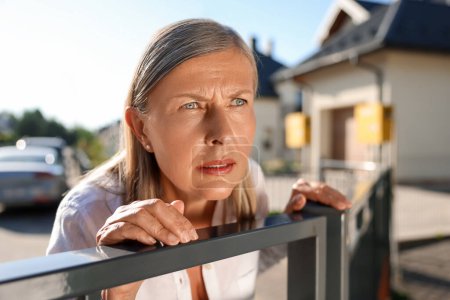 Photo for Concept of private life. Curious senior woman spying on neighbours over fence outdoors - Royalty Free Image