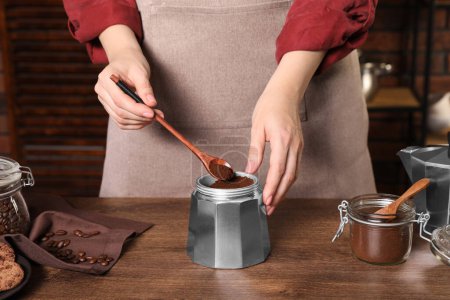 Woman putting ground coffee into moka pot at wooden table, closeup