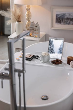Téléchargez les photos : Plateau en bois blanc avec tablette, lecteur cassette et bougies allumées sur la baignoire dans la salle de bain - en image libre de droit