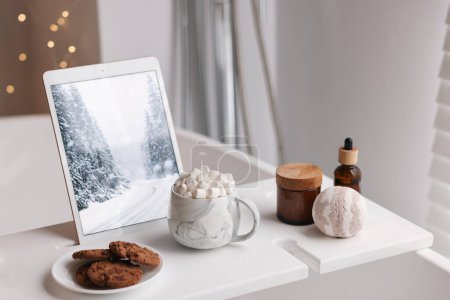 Téléchargez les photos : Plateau en bois blanc avec tablette, biscuits et produits de spa sur baignoire dans la salle de bain - en image libre de droit