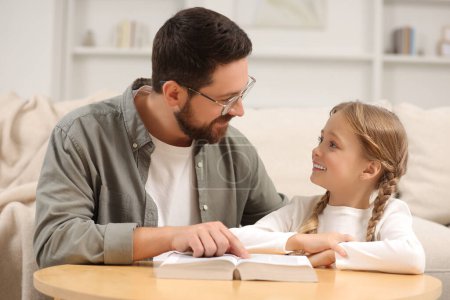Photo for Girl and her godparent reading Bible together at table in room - Royalty Free Image