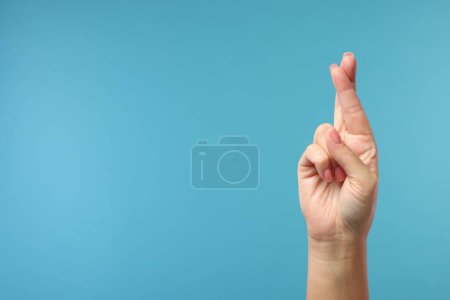 Foto de Mujer cruzando los dedos sobre fondo azul claro, primer plano. Espacio para texto - Imagen libre de derechos