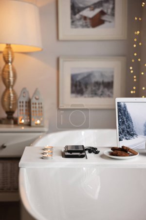 Téléchargez les photos : Plateau en bois blanc avec tablette, lecteur cassette, biscuits et bougies allumées sur la baignoire dans la salle de bain - en image libre de droit