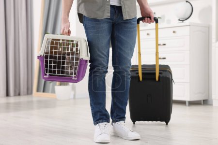 Téléchargez les photos : Voyage avec animal de compagnie. Homme tenant transporteur avec chat mignon et valise à la maison - en image libre de droit