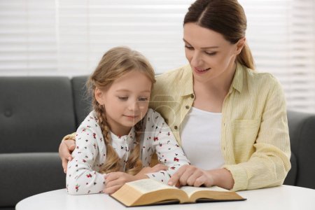Photo for Girl and her godparent reading Bible together at table indoors - Royalty Free Image