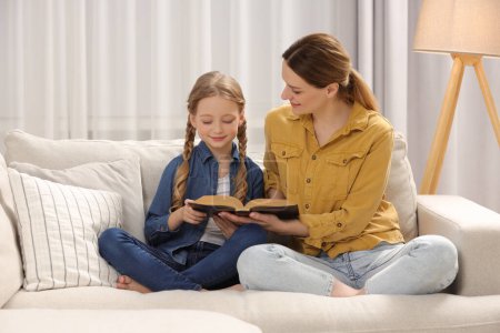 Photo for Girl and her godparent reading Bible together on sofa at home - Royalty Free Image