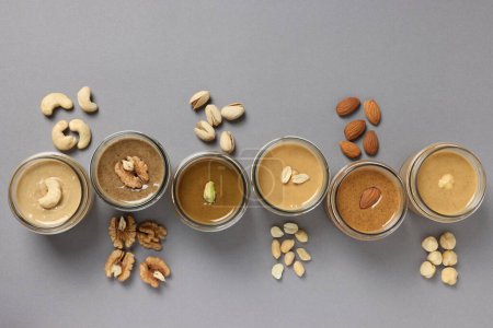 Photo for Tasty nut butters in jars and raw nuts on gray table, flat lay - Royalty Free Image