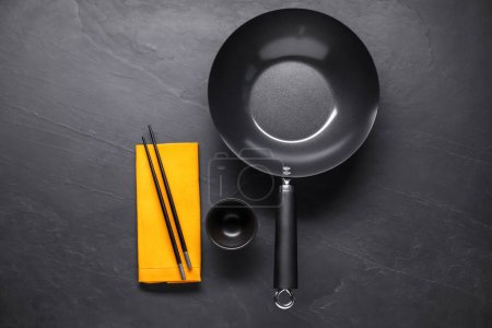 Photo for Empty iron wok, sauce bowl and chopsticks on black table, flat lay - Royalty Free Image