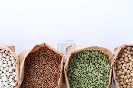 Téléchargez les photos : Différents types de légumineuses et de céréales dans des sacs en papier sur fond blanc, vue de dessus. Grains biologiques - en image libre de droit