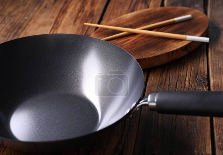 Photo for Empty iron wok and chopsticks on wooden table, closeup - Royalty Free Image