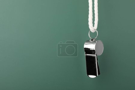 Referee equipment. Metal whistle on dark green background, closeup and space for text