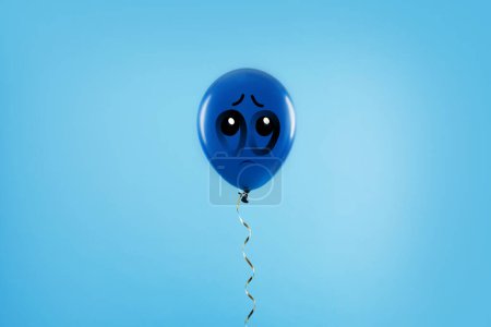Blauer Ballon mit traurigem Gesicht auf hellblauem Hintergrund