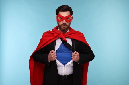 Foto de Hombre de negocios confiado que usa traje de superhéroe bajo traje sobre fondo azul claro - Imagen libre de derechos
