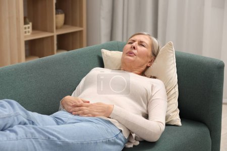 Téléchargez les photos : Ménopause. Femme souffrant de douleurs abdominales sur le canapé à la maison - en image libre de droit
