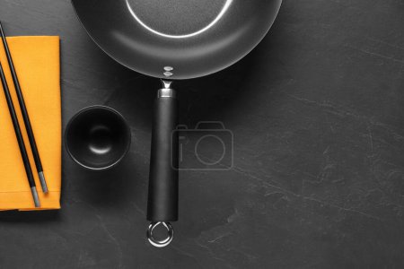 Photo for Empty iron wok, sauce bowl and chopsticks on black table, flat lay. Space for text - Royalty Free Image