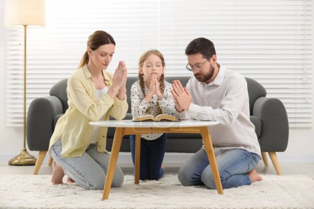 Foto de Chica y sus padrinos orando sobre la Biblia juntos en la mesa en el interior - Imagen libre de derechos
