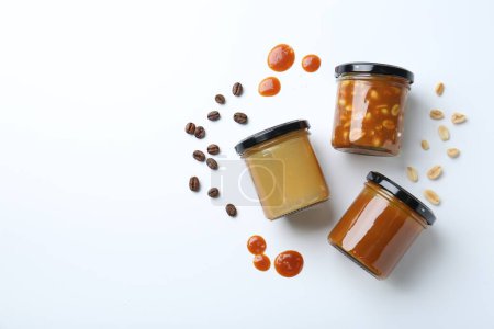 Photo for Tasty salted caramel in jars with peanuts and coffee beans on white background, flat lay. Space for text - Royalty Free Image